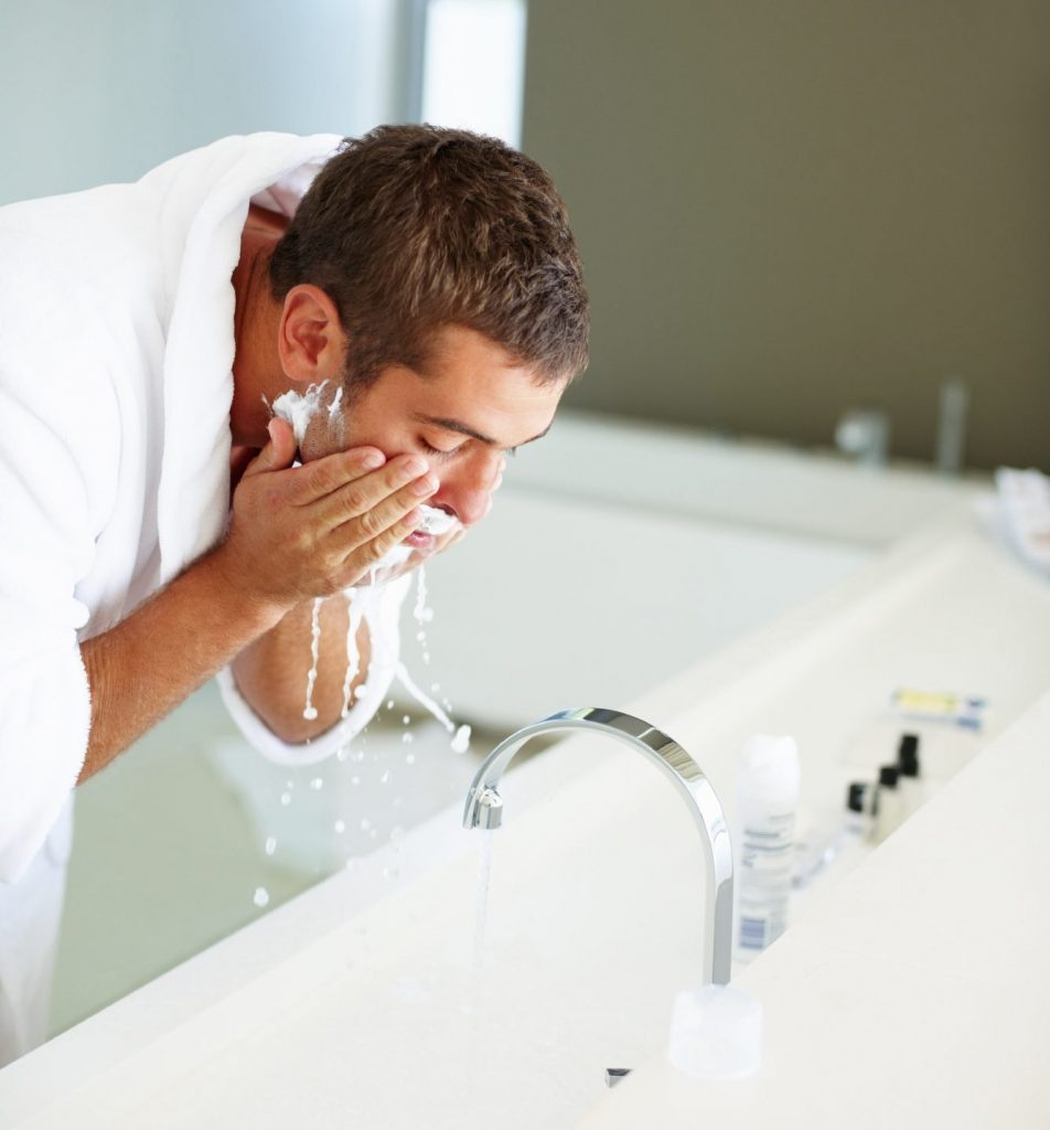 Homme qui se lave le visage dans la salle de bain