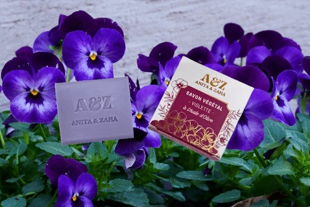 Photo du Savon Végétal Violette ANITA & ZAHA présenté avec un arrière-plan de fleurs violettes naturelles – © ANITA & ZAHA